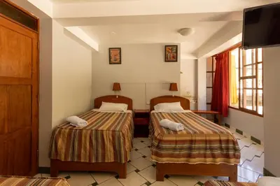 a hotel room with two beds and a television at Hostal La Payacha MachuPicchu in Machu Picchu