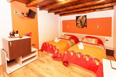 two beds in a room with orange walls and wooden floors at Casona les Pleiades in Cusco