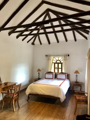 a bedroom with a bed and a table and a window at Las Casitas del Arco Iris in Urubamba