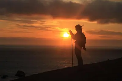 a woman standing on the beach with ski poles at sunset at AQUAMARINE PARACAS Beach Hostal in Paracas