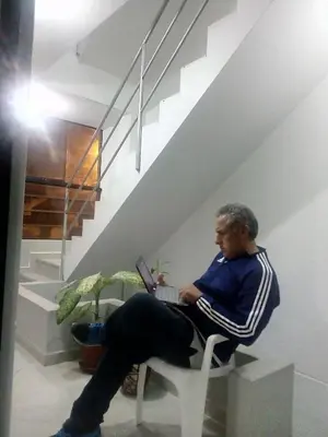 a man sitting in a chair under a staircase with a laptop at Sunset Hostel Airport in Lima
