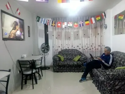 a man sitting on a couch in a living room with a laptop at Sunset Hostel Airport in Lima