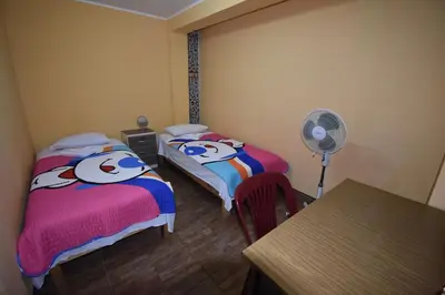 two beds in a room with a fan and a table at El Viajero Aeropuerto in Lima