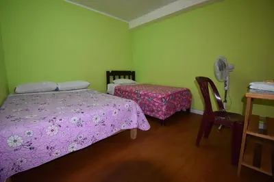 a bedroom with two beds and a fan and a table at El Viajero Aeropuerto in Lima