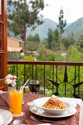 a table with a plate of pasta and a glass of orange juice at Hotel Mabey Urubamba in Urubamba