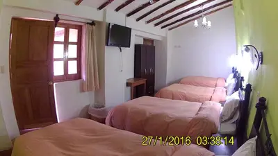 a bedroom with two beds and a tv on the wall at Hostal Qorichaska in Cusco