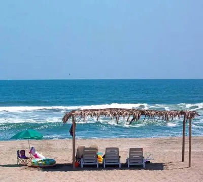 a woman sitting in a chair under an umbrella on the beach at Topara Hotel Boutique in San Vicente de Cañete