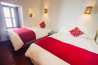 two beds in a room with red and white sheets at Rumi Wasi in Cusco