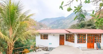 a small white house with mountains in the background at Eco Hacienda Roman in Machu Picchu