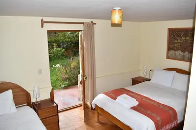 a bedroom with two beds and a door to a garden at Apu Lodge in Ollantaytambo