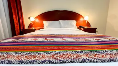 a bed with a colorful blanket on it with two lamps at La Mansion Casa Hotel in Andahuaylas
