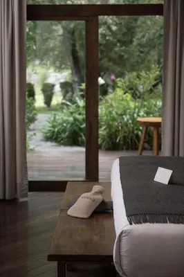 a bed with a slippers on a table next to a window at Andenia Boutique Hotel, Sacred Valley in Urubamba