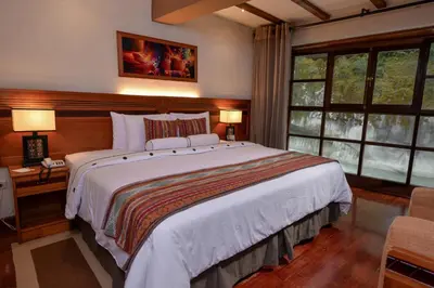 a bedroom with a large bed and two windows at Casa del Sol Machupicchu in Machu Picchu