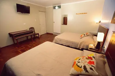 a hotel room with two beds and a bench at Hospedaje Zaragoza in Ayacucho