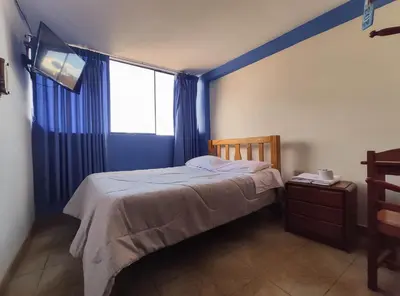 a bedroom with a bed with blue curtains and a window at Hospedaje Manchego's in Huancayo