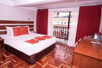 a bedroom with a bed and a desk and a balcony at Hotel Arcangel in Cusco