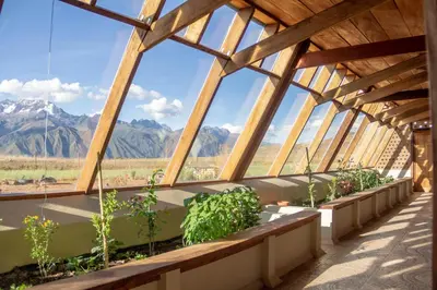a greenhouse with plants and mountains in the background at Casa 100% ecológica con vista a los glaciares andinos in Maras