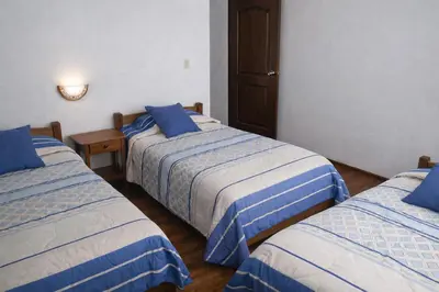 three beds in a room with blue and white sheets at Hostal Arias in Oxapampa