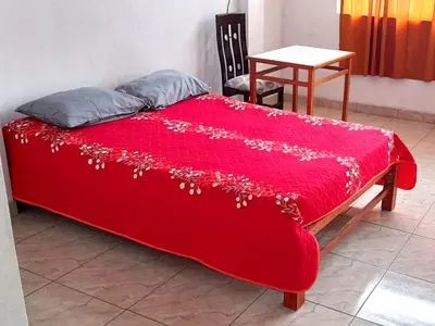a red bed with a red blanket with a table at Hospedaje Arana in Chincha Alta
