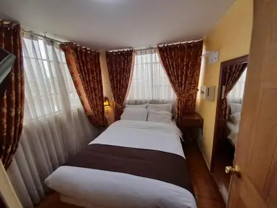 a small bedroom with two beds in front of windows at CasaHotel Centro - Huancayo in Huancayo