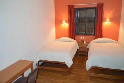 two beds in a room with orange walls and a window at Hotel Casa Campesina in Cusco
