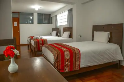 a hotel room with two beds and a vase with flowers at Hotel Del Prado Hometown in Cusco