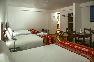 a hotel room with three beds and a table at Hotel Del Prado Hometown in Cusco