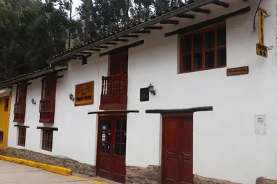 a white building with wooden doors and windows at Wayras Hostal in Ollantaytambo