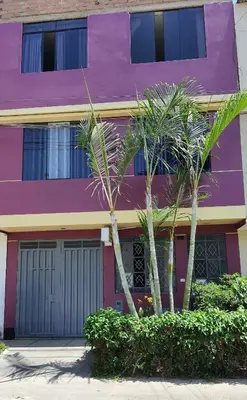 a purple building with two palm trees in front of it at EL TUMI - Aeropuerto in Lima