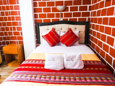 a bed with red and white pillows and a brick wall at Hostal Encanto Machupicchu in Machu Picchu