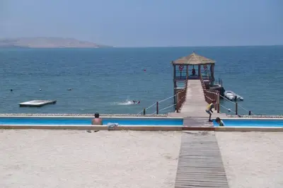a wooden boardwalk leading to the ocean with people on the beach at PARACAS megaview bayfront flat in Paracas