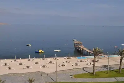 a beach with chairs and a pier with boats in the water at PARACAS megaview bayfront flat in Paracas