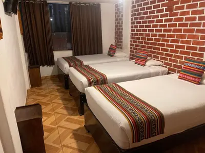 three beds in a room with a brick wall at Quipu Hostal in Machu Picchu