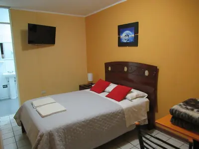 a bedroom with a bed with red pillows and a television at Kurmi Hostel Lima Airport in Lima