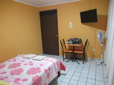 a bedroom with a bed and a table and a tv at Kurmi Hostel Lima Airport in Lima
