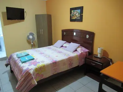 a bedroom with a bed with a dresser and a fan at Kurmi Hostel Lima Airport in Lima