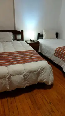 two beds in a room with wooden floors at KAARO HOUSE CUSCO in Cusco