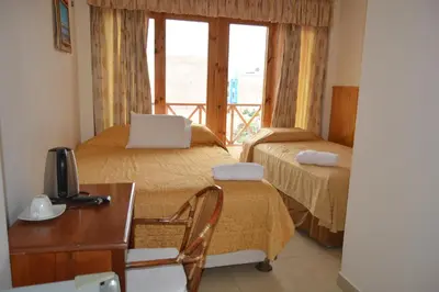 a room with two beds and a desk and a window at Hotel Los Flamencos in Paracas