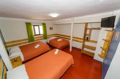 a small room with two beds and a television at Ukukus Hostel in Cusco