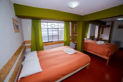 a small bedroom with two beds and a window at Ukukus Hostel in Cusco