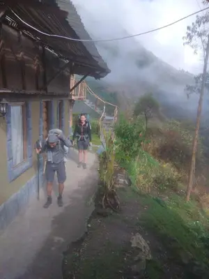two people walking down a path next to a house at Salkantay Hostel Chaullay in Santa Teresa