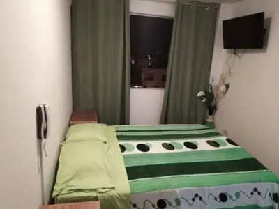 a bedroom with a bed with green sheets and a window at Hospedaje Kaihalulu in Punta Hermosa