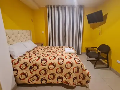 a bedroom with a bed and a chair and a window at Hostal Tuki Huancayo in Huancayo