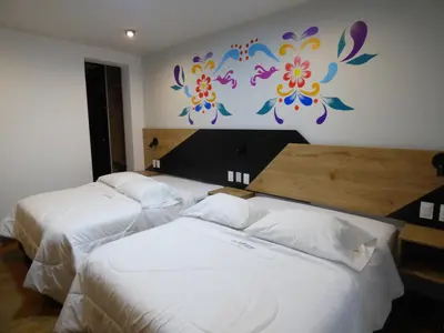 two beds in a hotel room with a mural on the wall at Platero Hotel in Ayacucho