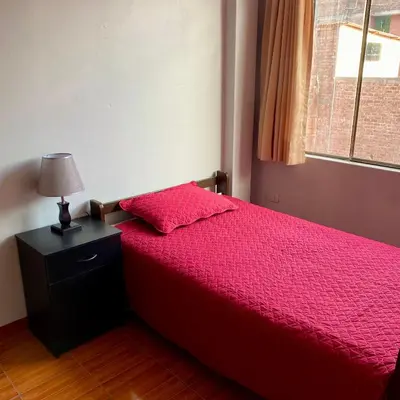 a bedroom with a red bed with a lamp and a window at Departamento céntrico con terraza ideal para grupos in Ayacucho