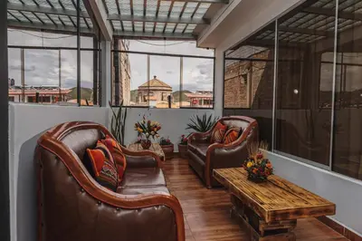 two leather chairs and a table in a room with windows at San Pedro Apartments in Cusco