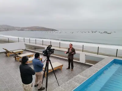 a man standing next to a swimming pool with a camera at Hotel Terrazas Del Mar in Huacho