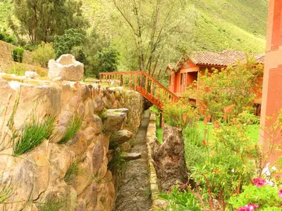 a garden with a rock wall and a wooden bridge at Tierra Viva Ollantaytambo in Ollantaytambo