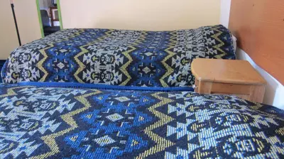 a bed with a blue and yellow blanket and a wooden table at Garden Inn 488 in Cusco