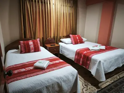 a hotel room with two beds with red and white sheets at Hotel Colquewasi in Cusco